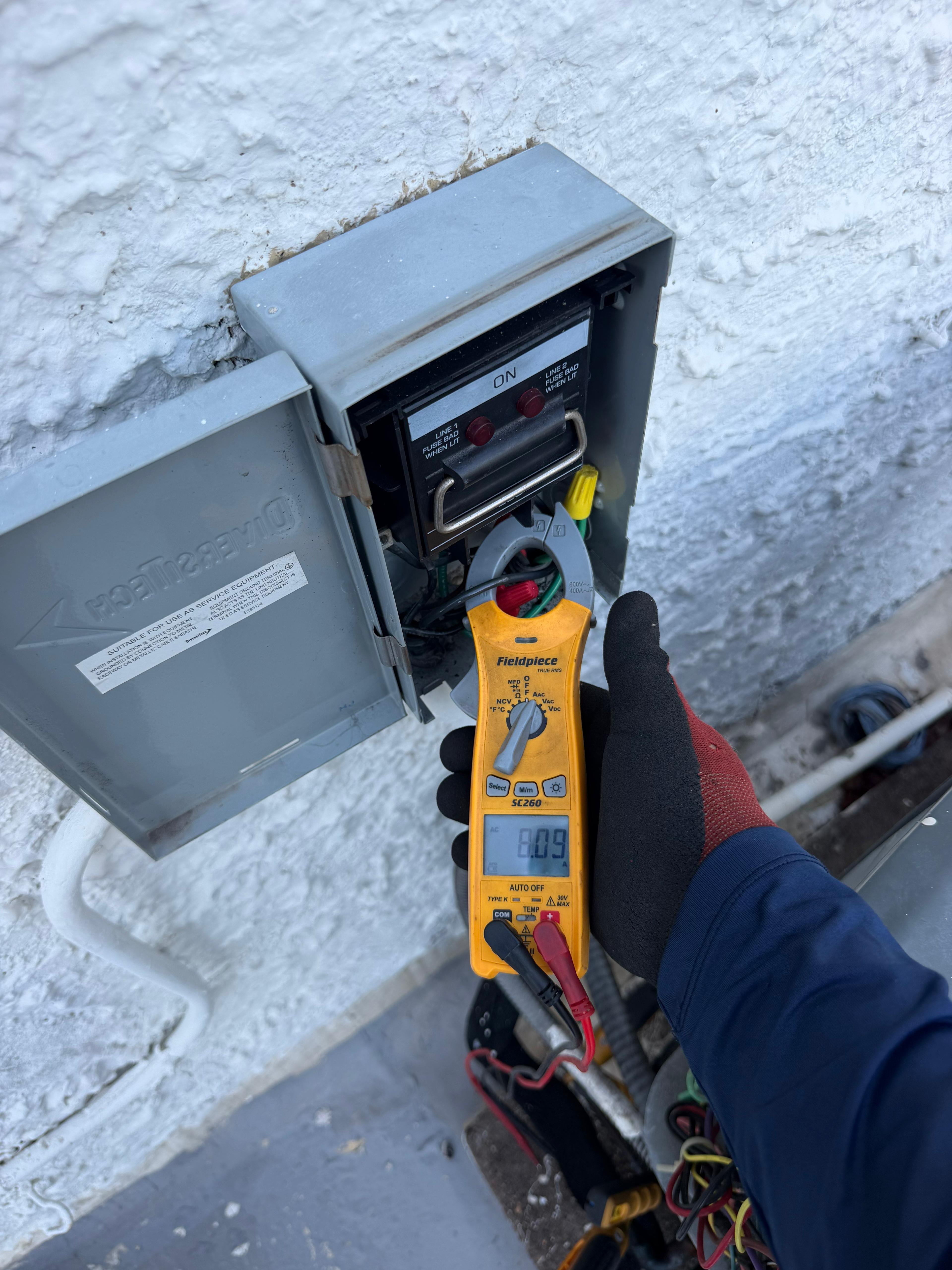 Cooling Masters technician using Fieldpiece SC260 clamp meter on AC disconnect panel